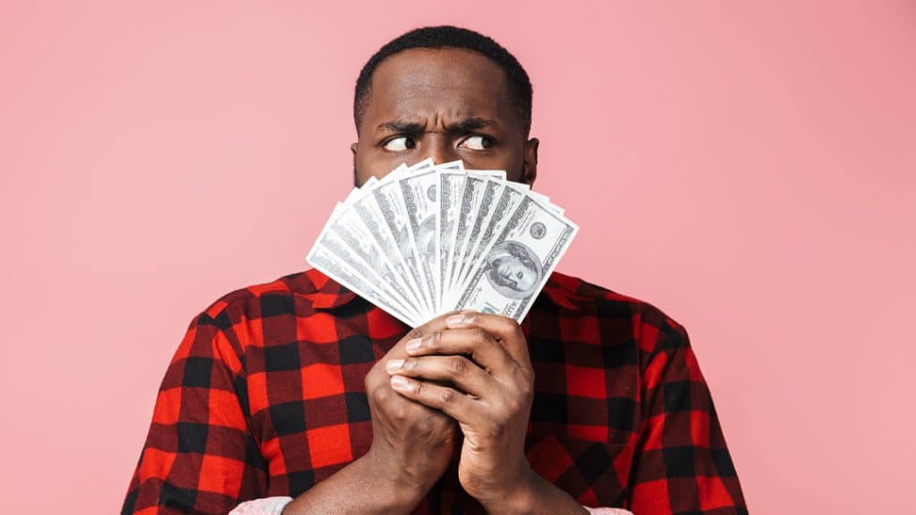 A man fans money in front of his face as he considers his savings options: get a share certificate, a cd or certificate of deposit, or a high-yield savings account. Decisions, decisions!