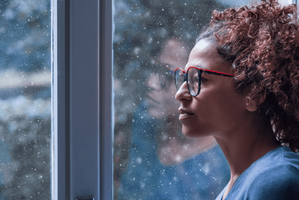Woman gazing at the snow as it falls outside while she ponders her holiday stress