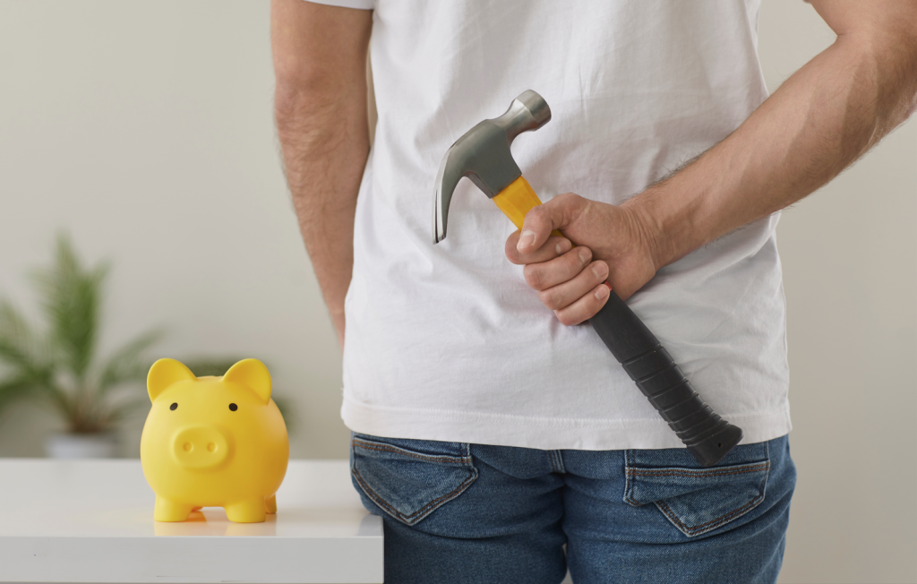 A man approaching his emergency fund with a hammer to access the money.